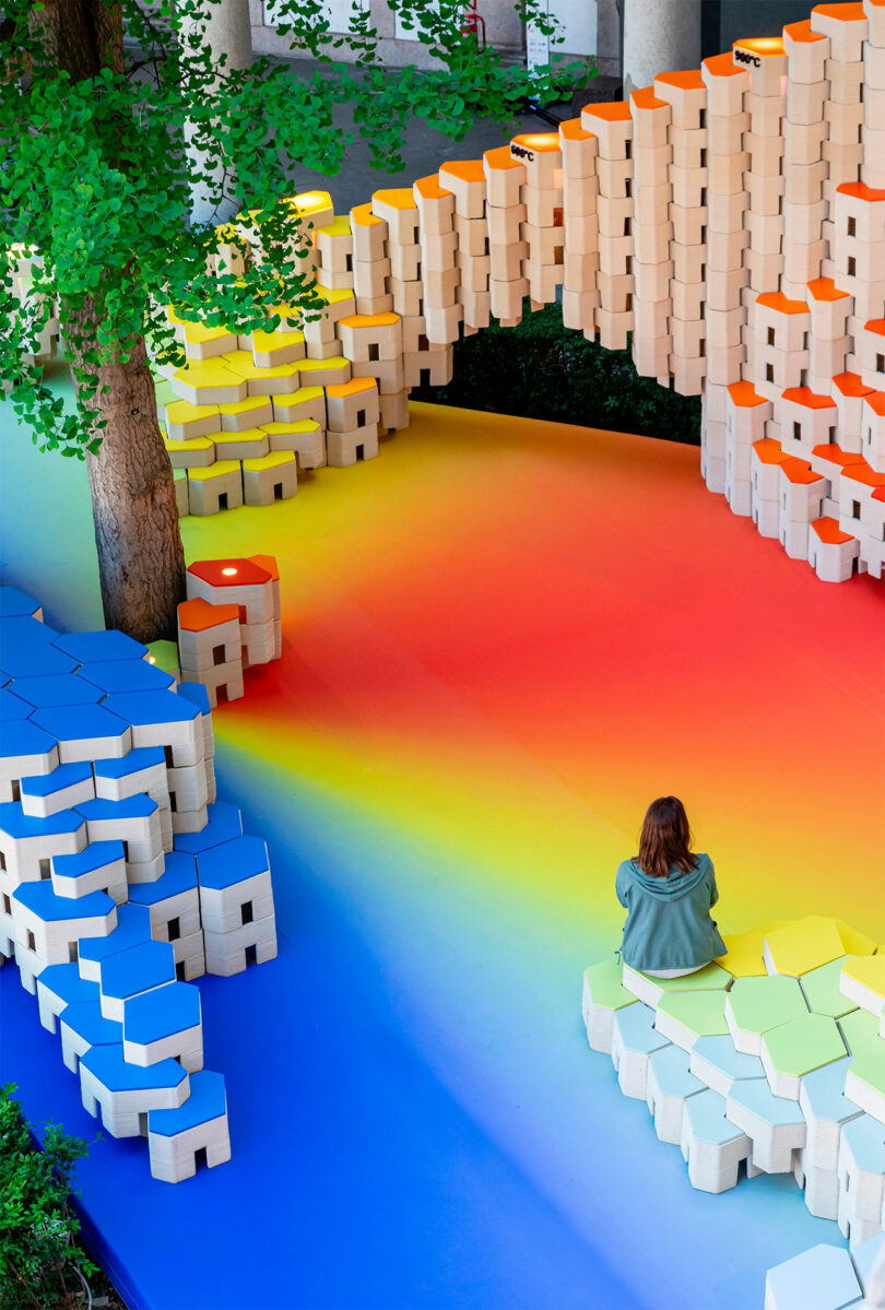 Art installation in a courtyard featuring a vibrant, cascading archway made of stacked colored blocks.