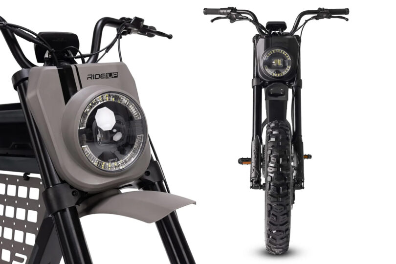 A close-up and full front view of a black Ride1Up Revv1 DRT eBike, highlighting the headlight and tire. The bike has a robust design with a geometric frame and a wide tread tire.