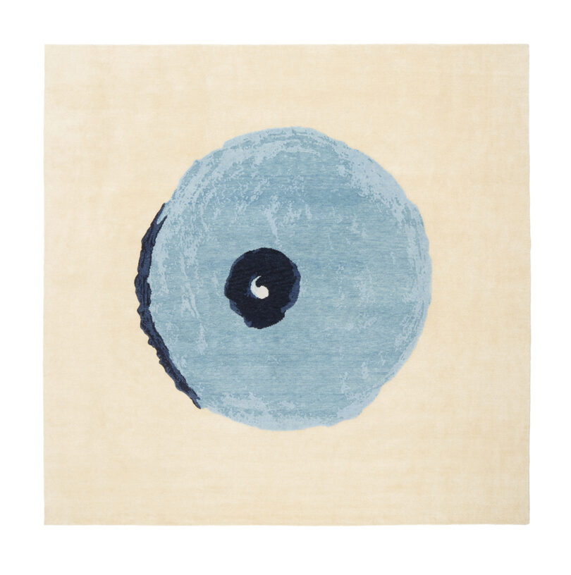 A square rug featuring a large, stylized circular blue and black design centered on a beige background.