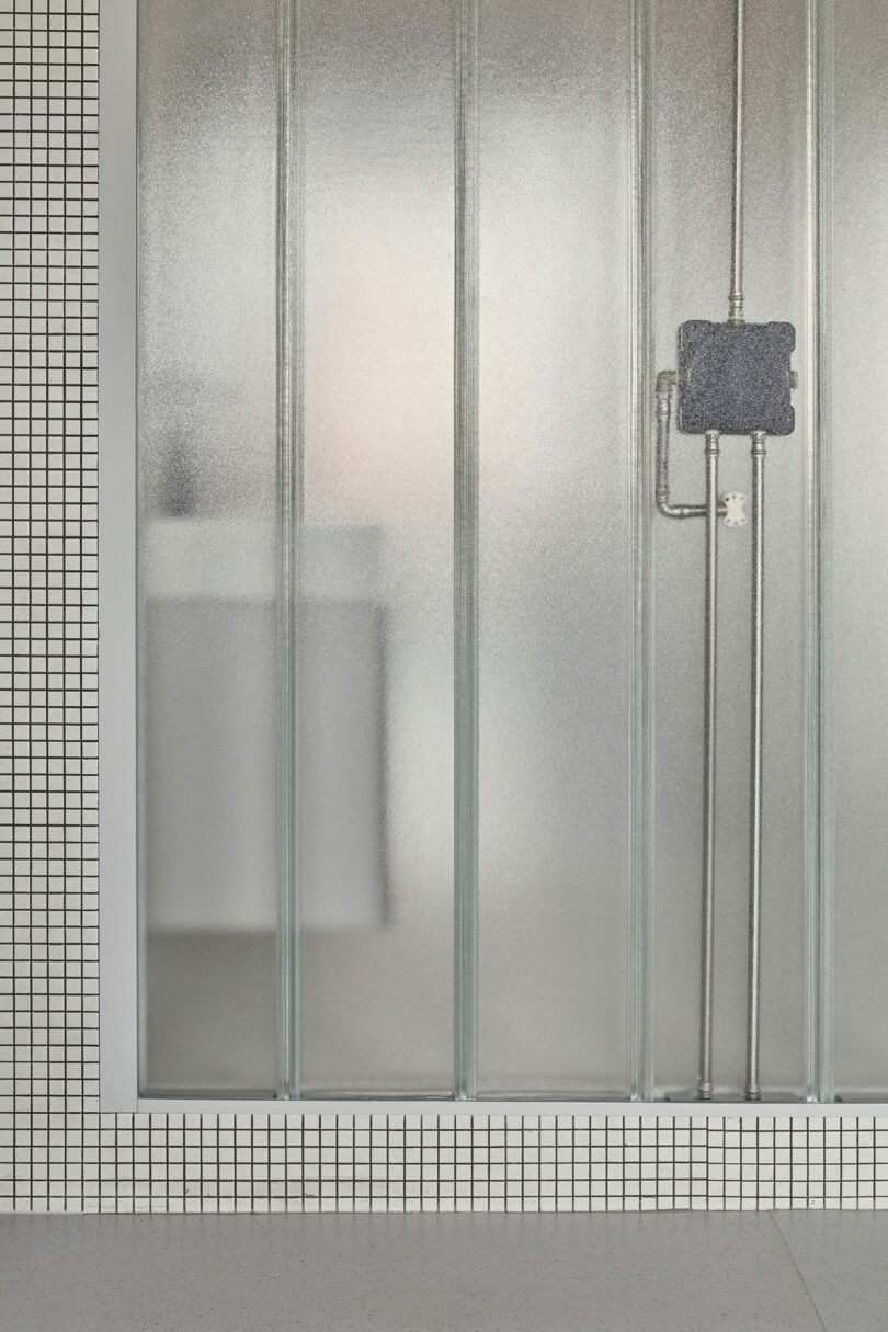 A frosted glass shower enclosure with visible plumbing and a tiled wall.