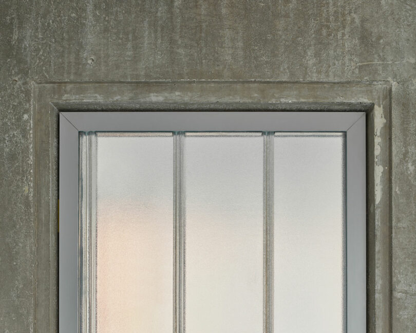 A frosted glass window with vertical metal bars set in a concrete wall.