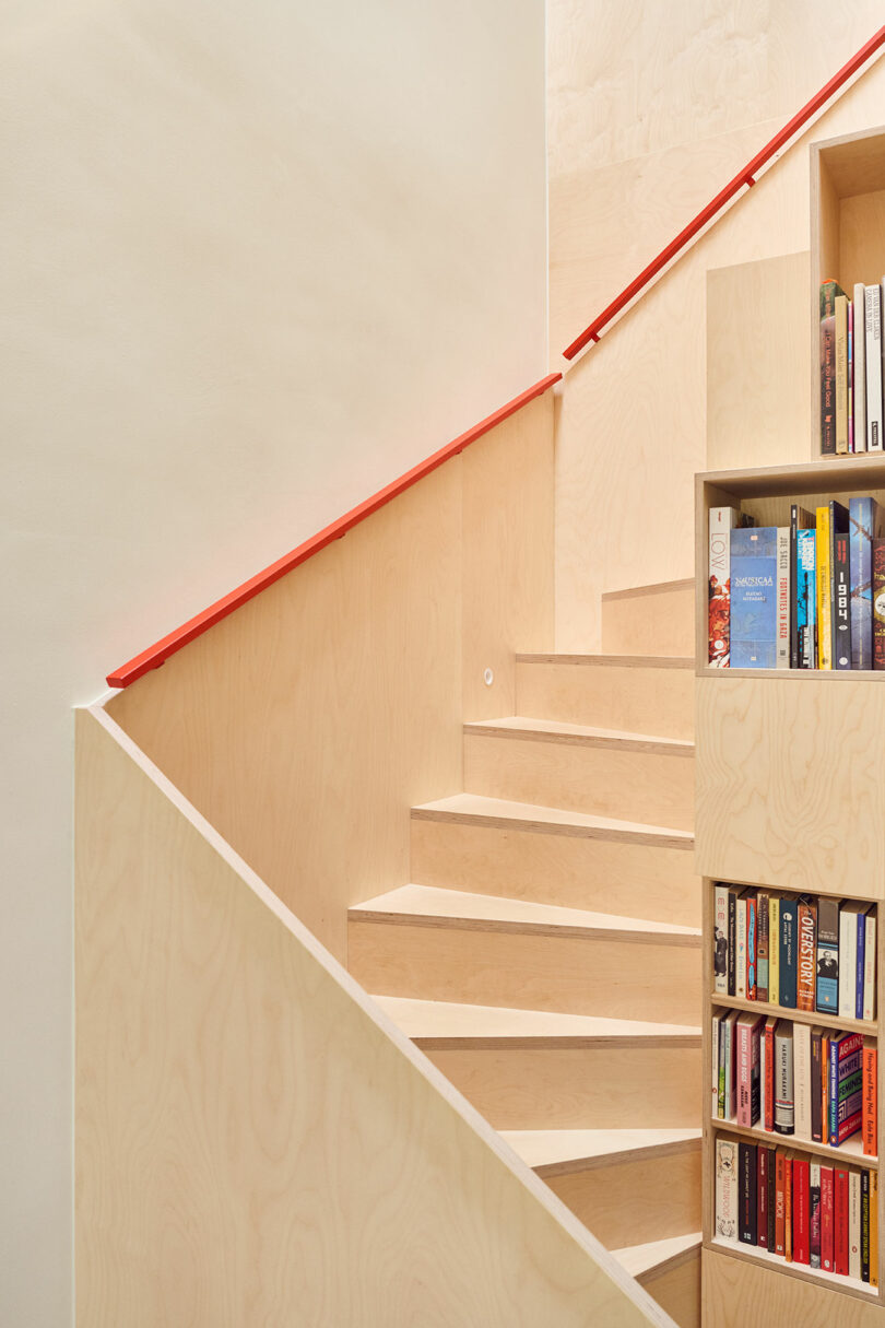 A wooden staircase with a red handrail features built-in shelves filled with a variety of books.