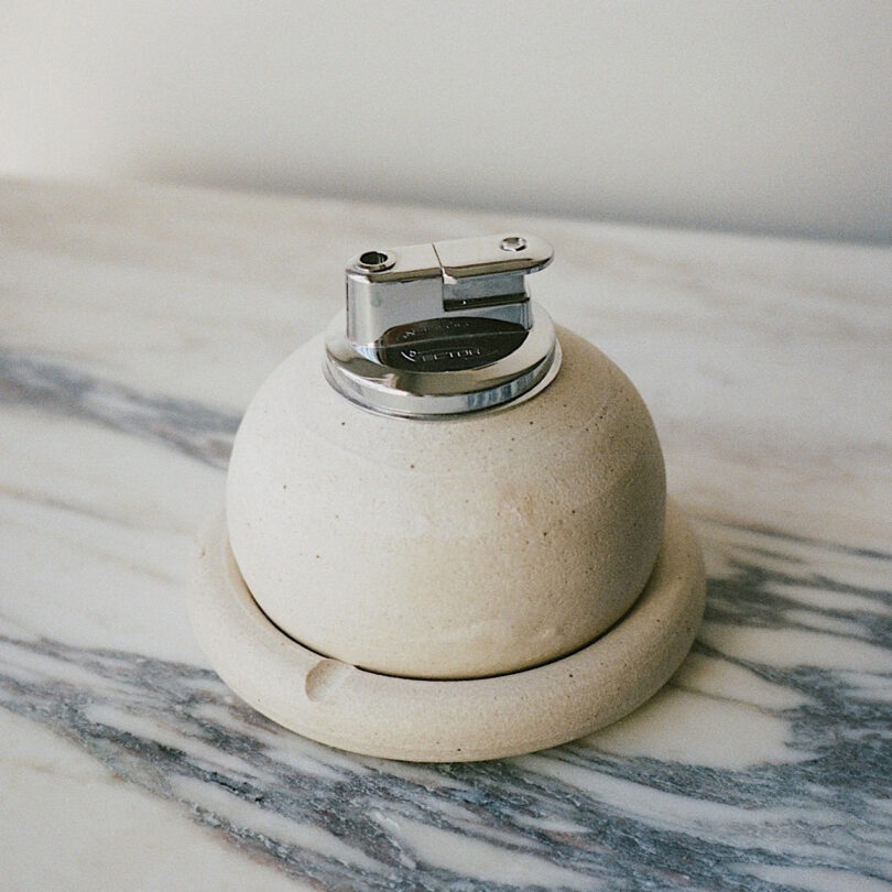 A lighter sits atop a concrete ashtray base on a marbled surface.