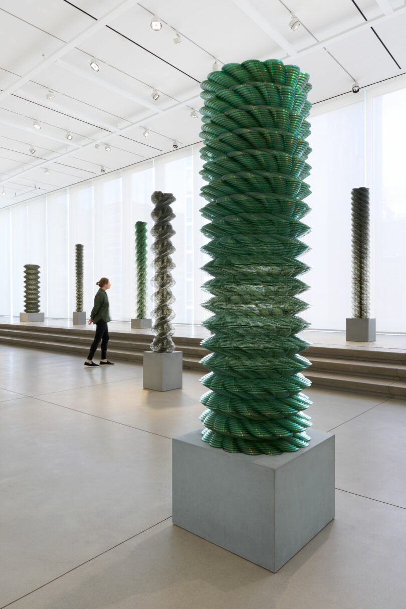 Woman admires gallery full of columns made from CDs by Tara Donovan