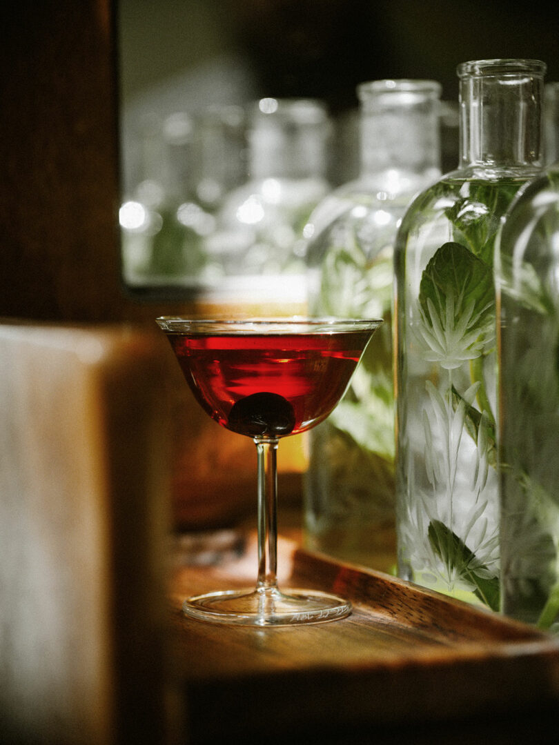 Styled shot of a modern martini glass filled with dark red liquid in front of glass bottles
