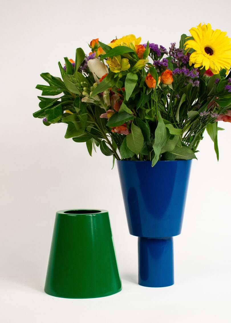 A bundle of colorful flowers in a two-piece blue and green vase, set against a plain white background.