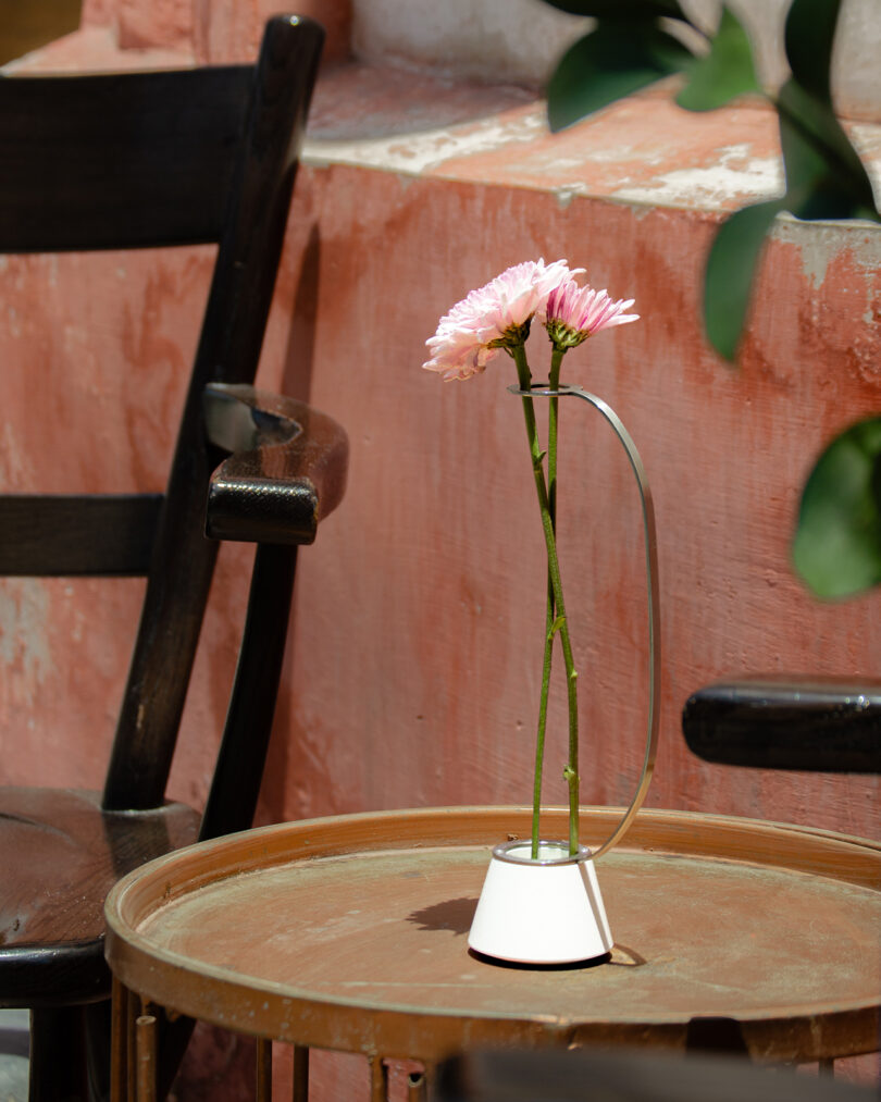 A single pink flower in a minimalistic vase on a round wooden table.