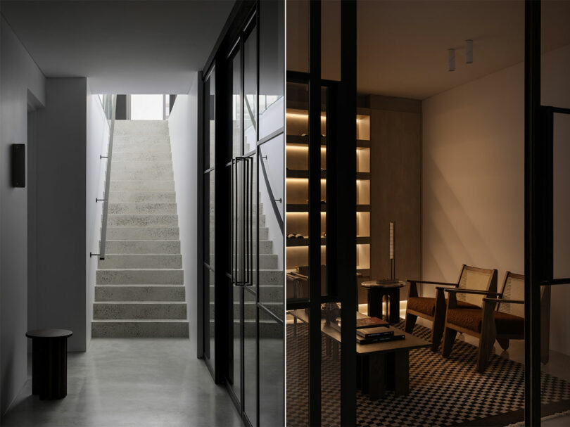 A modern interior featuring a minimalist staircase with glass railings on the left and a dimly-lit lounge area with bookshelves and wooden chairs on the right.