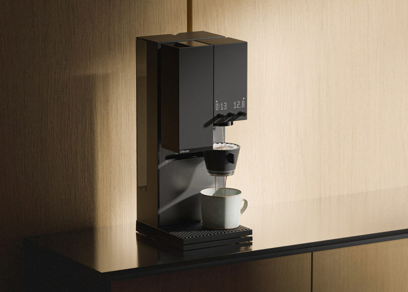 Modern xBloom Studio coffee maker dispensing coffee into a cup, set against a wooden kitchen backdrop.