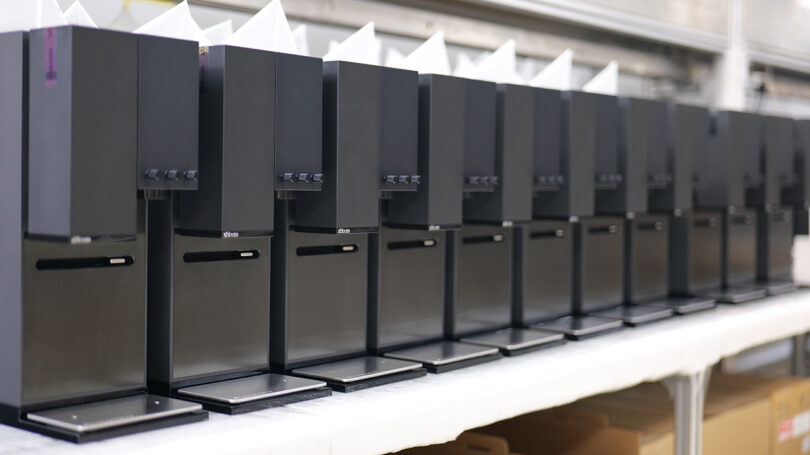 A line up of ten preproduction xBloom Studio coffee makers in midnight black finish.