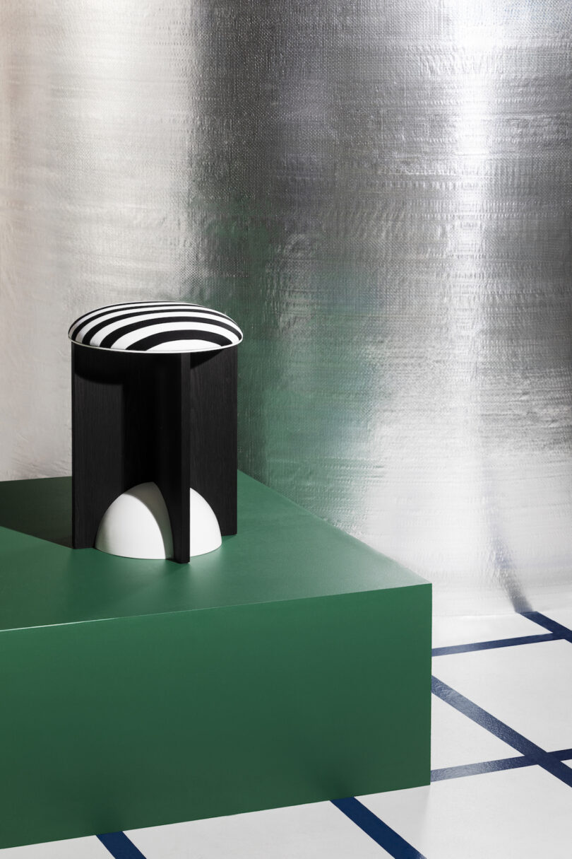 A green cylindrical stool with black and white upholstery on a green pedestal
