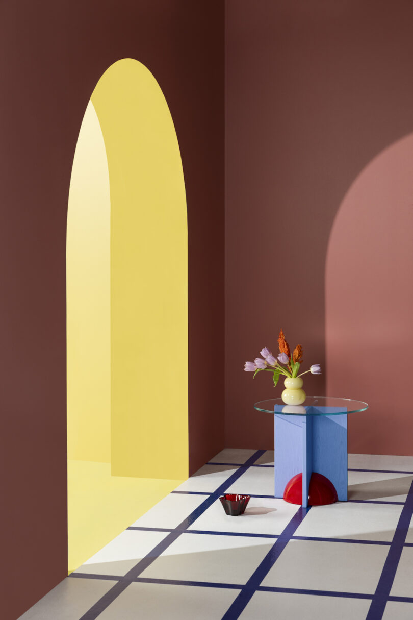 A colorful interior featuring a yellow arched doorway, a blue table with a vase of flowers, and a geometric floor pattern