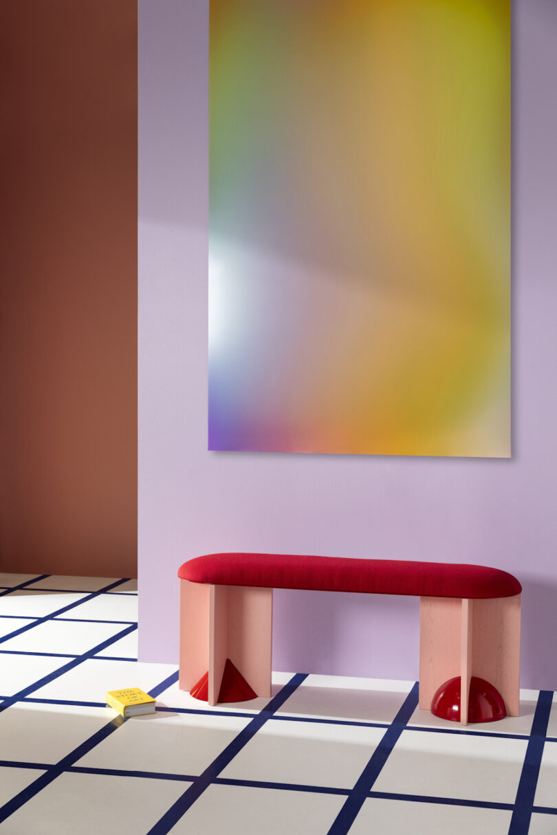 Abstract blur painting on a wall above a red and pink bench, positioned on a white and blue geometric tiled floor with a book beside the bench
