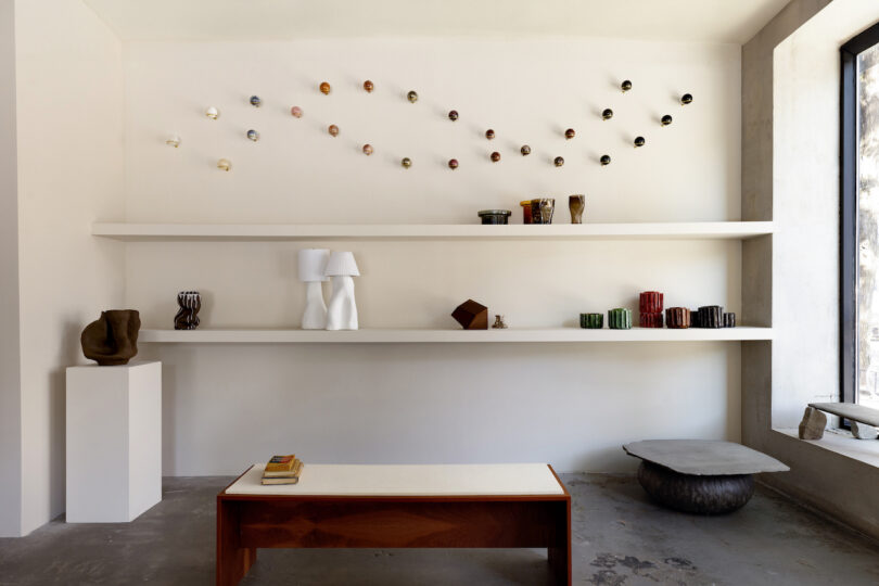 A minimalist room with floating shelves displaying various artistic objects, including a display of spheres of natural stones hanging above the shelf
