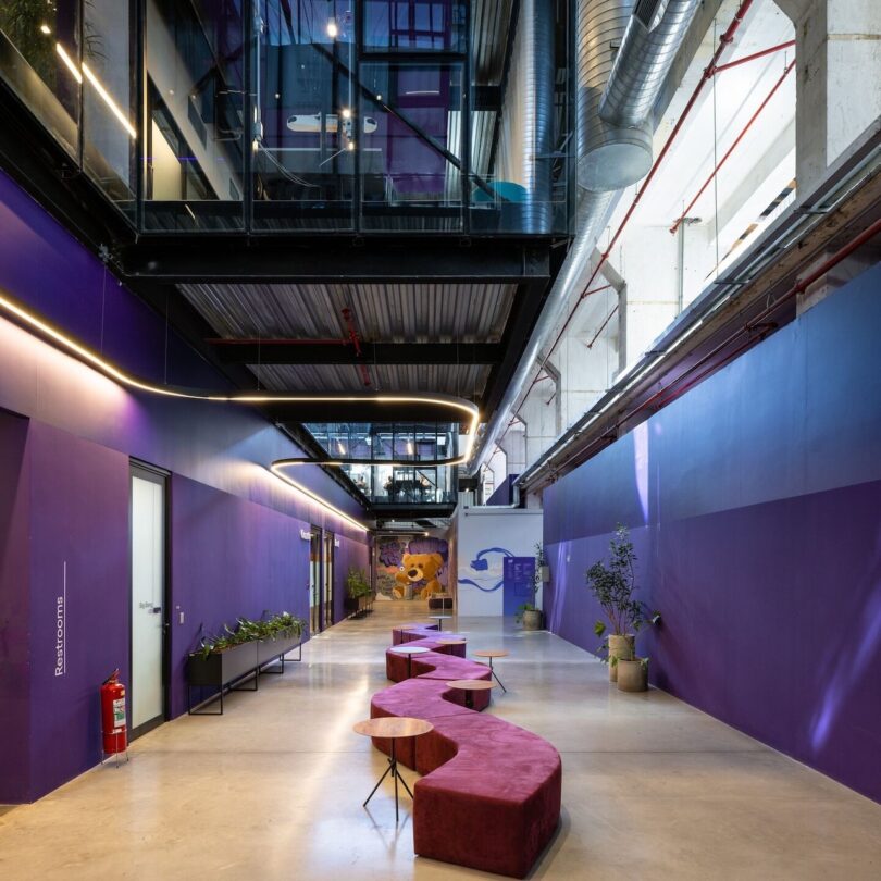 Modern office hallway with purple walls, red bench seating, and green plants. Industrial ceiling with exposed ductwork