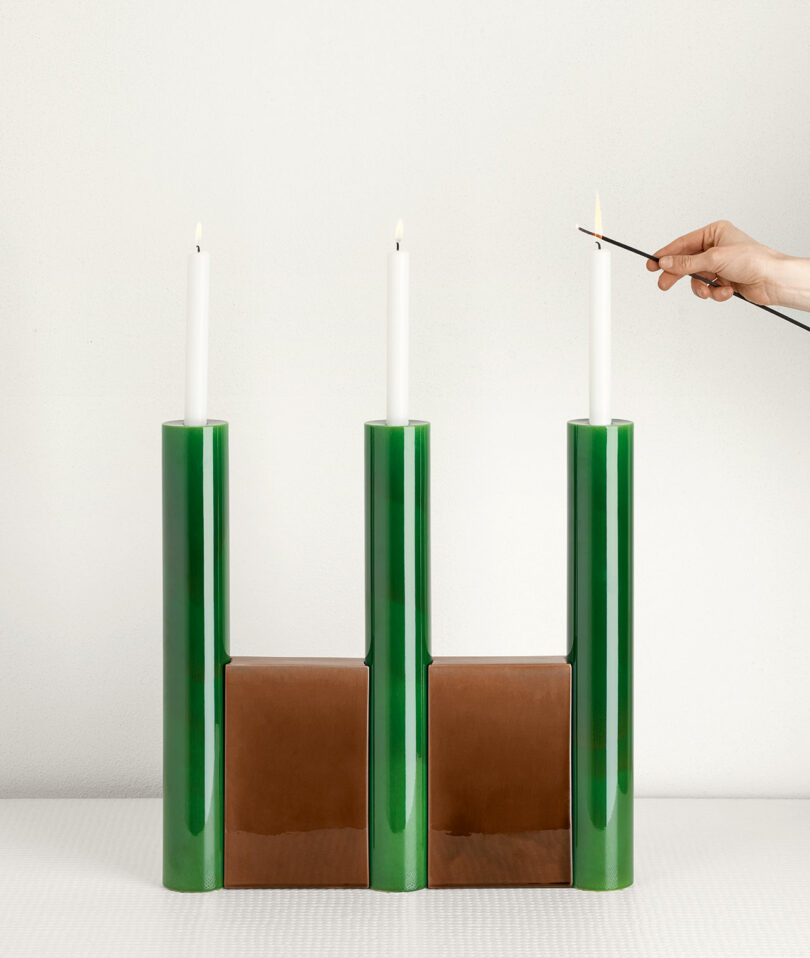 hand lighting a candle held in place by a green and brown candelabra