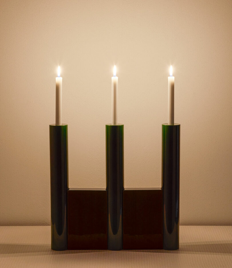 three lit candles held in place by a green and brown candelabra