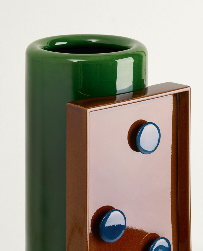  a green cylindrical vase with a rectangular brown and blue section attached.