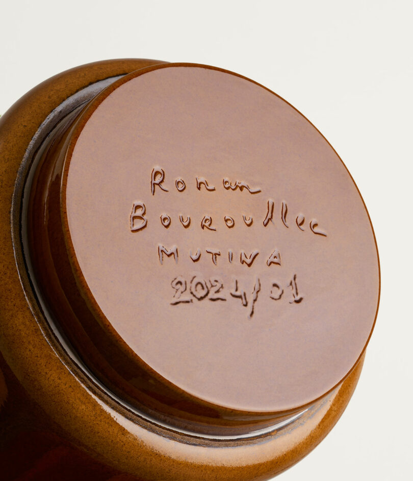 A close-up view of the bottom of a brown ceramic object. The base is inscribed with "Ronan Bouroullec Mutina 2024 / 01