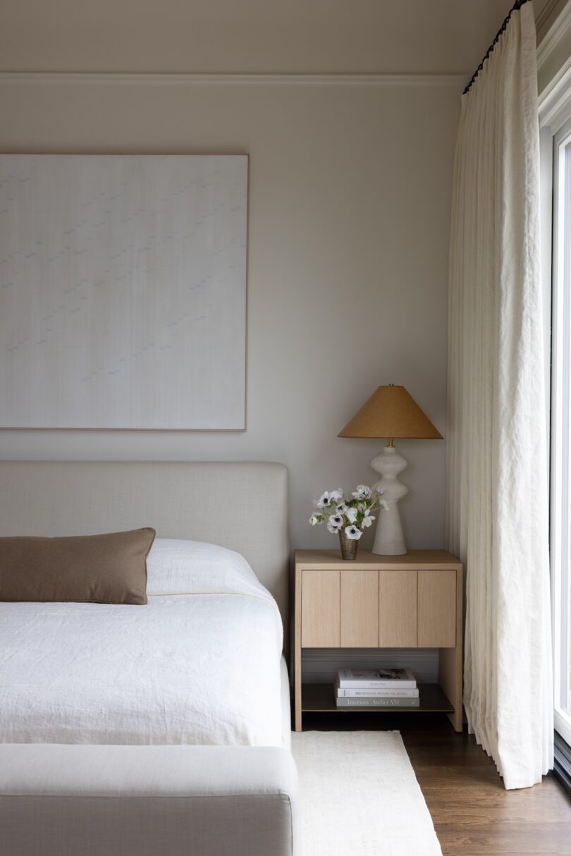 A minimalist bedroom featuring a light beige upholstered bed with white linens and a brown accent pillow.