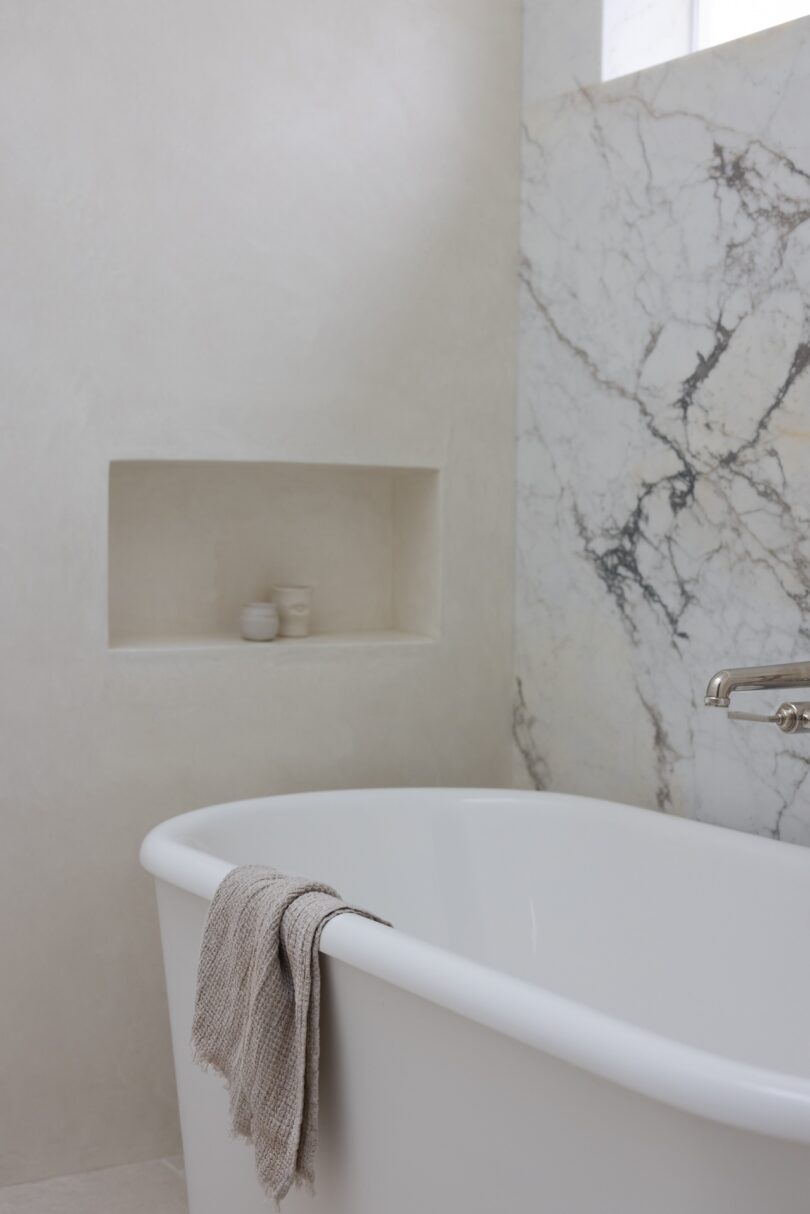 A minimalist bathroom featuring a white freestanding bathtub with a gray towel draped over the edge.