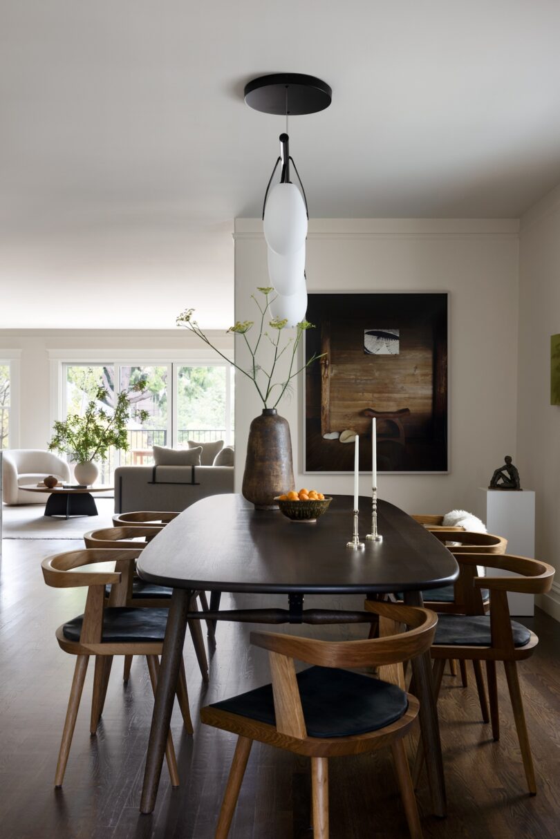 A contemporary dining room with a dark wood table and six modern wooden chairs with black seat cushions.