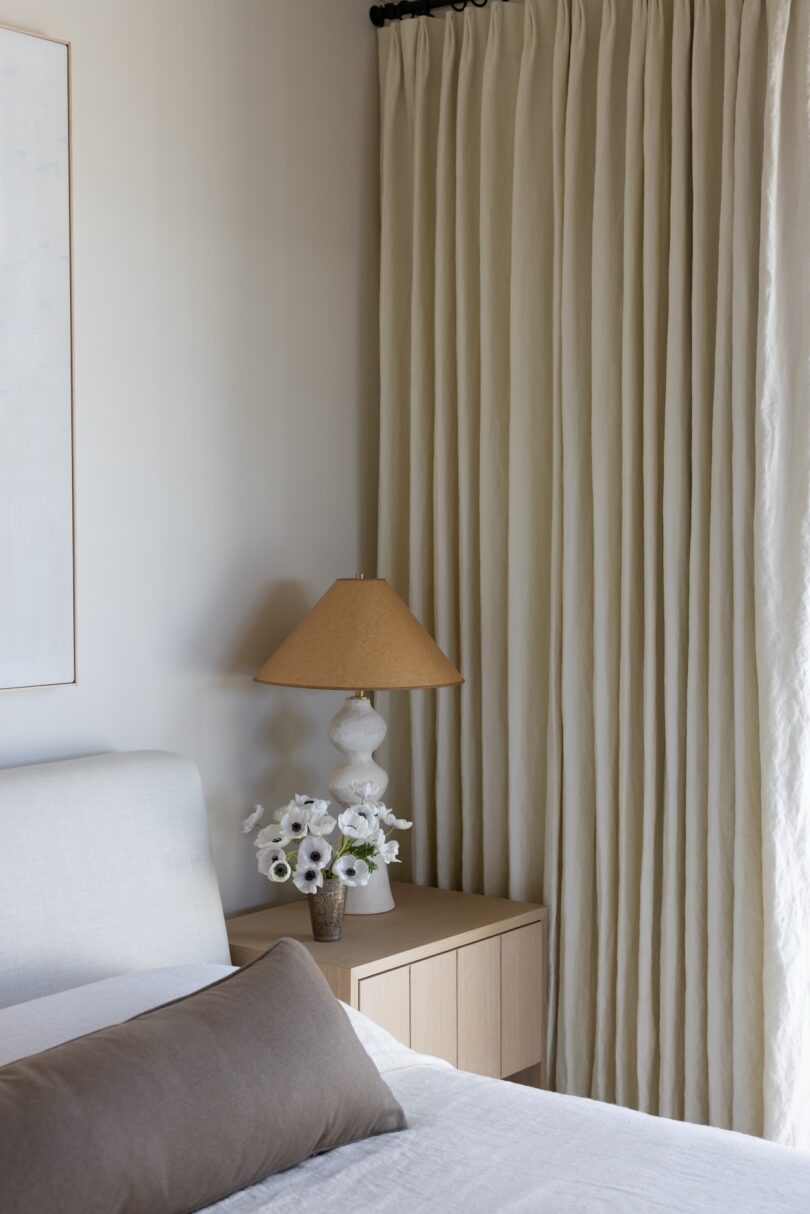 A serene bedroom with light beige walls and an upholstered bed with white linens. 