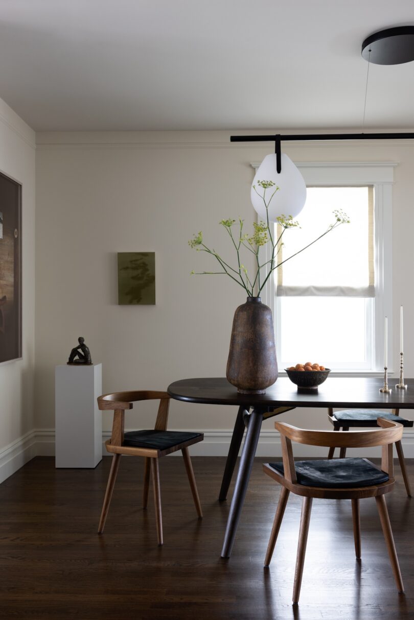 A contemporary dining room with a round dark wood table and four modern wooden chairs with black seat cushions.