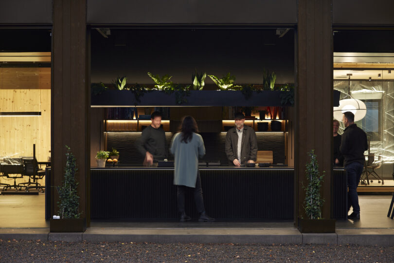 People interacting at a modern office kitchen with wooden paneling and ambient lighting at dusk