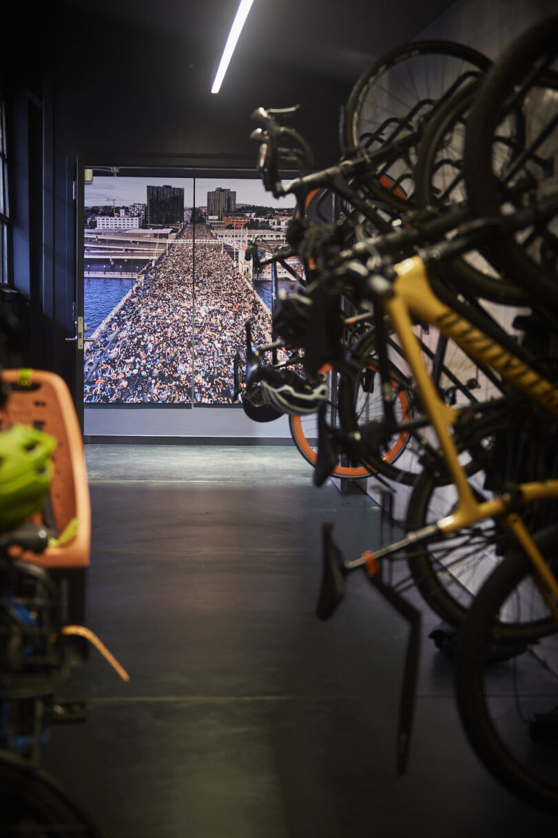 View from a dimly lit bike storage room looking out to a brightly lit stadium full of spectators; bikes hang on the right