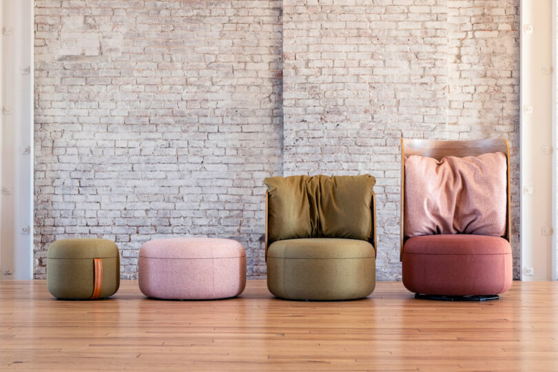 Four modern cushioned seats of varying sizes and colors are arranged in front of a brick wall. The seats include two ottomans, a chair without arms, and a chair with a wooden backrest