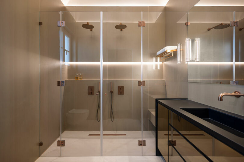 Modern bathroom featuring a double walk-in shower with glass doors and rain showerheads, a black countertop with built-in sink, and warm lighting.