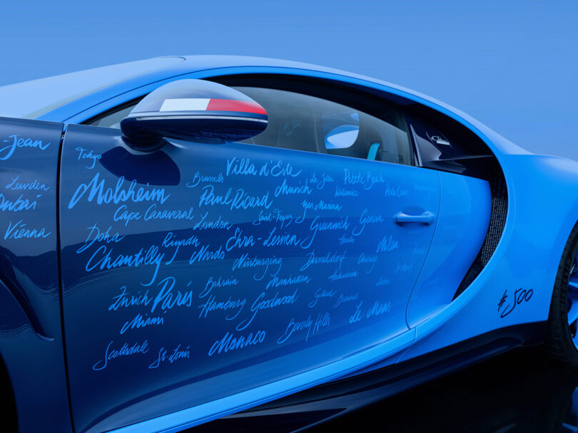 Close-up of a blue Bugatti Chiron door adorned with numerous handwritten signatures or names, featuring a side mirror partially wrapped with the French flag.