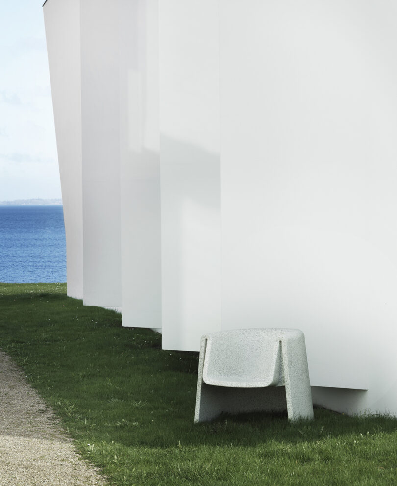 A streamlined white chair is placed on the grass near the sea.