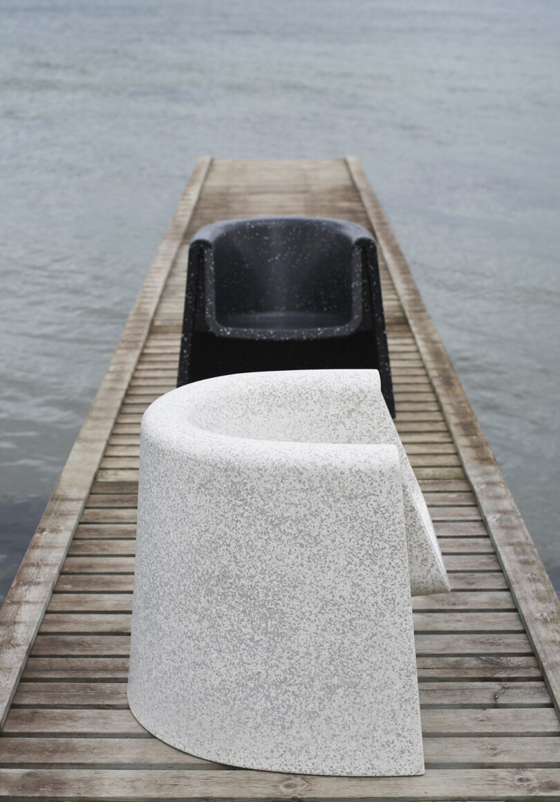 Two minimalist, modern chairs on a dock. One is black with white speckles and the other is white. Both have a smooth, curved design.