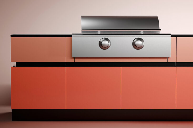 A modern outdoor kitchen countertop with coral-colored cabinets and a built-in stainless steel grill with two knobs.