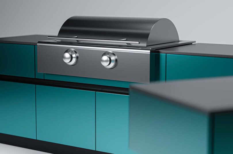 A modern outdoor kitchen setup with a stainless steel grill featuring two knobs, surrounded by blue-green cabinets.