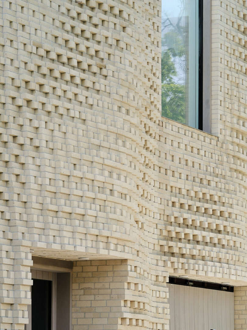 Close-up of a building facade featuring a unique, wavy, textured pattern made of light-colored bricks, with a large vertical window and part of a doorway visible.