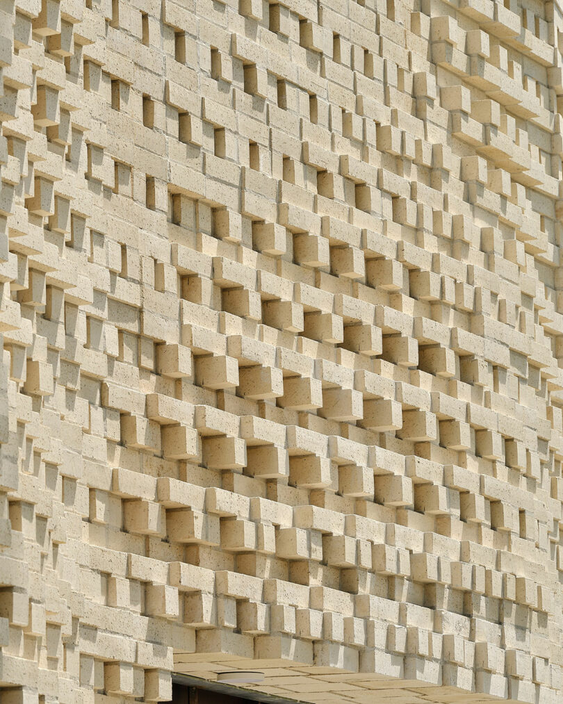 A building façade made of beige stone blocks arranged in a geometric, stepped pattern.