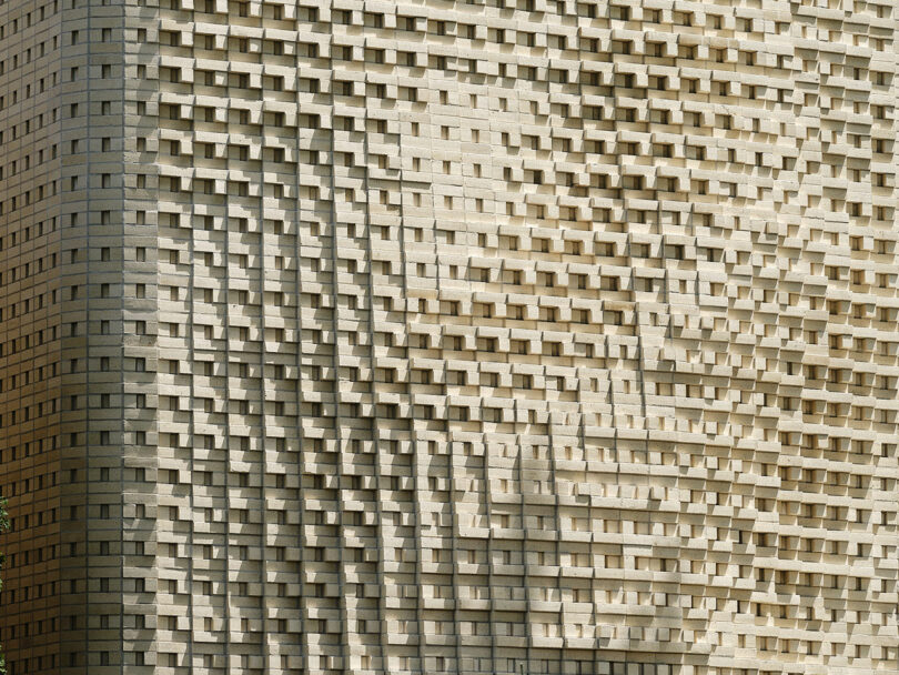 A close-up view of a beige brick wall with a textured, undulating pattern.