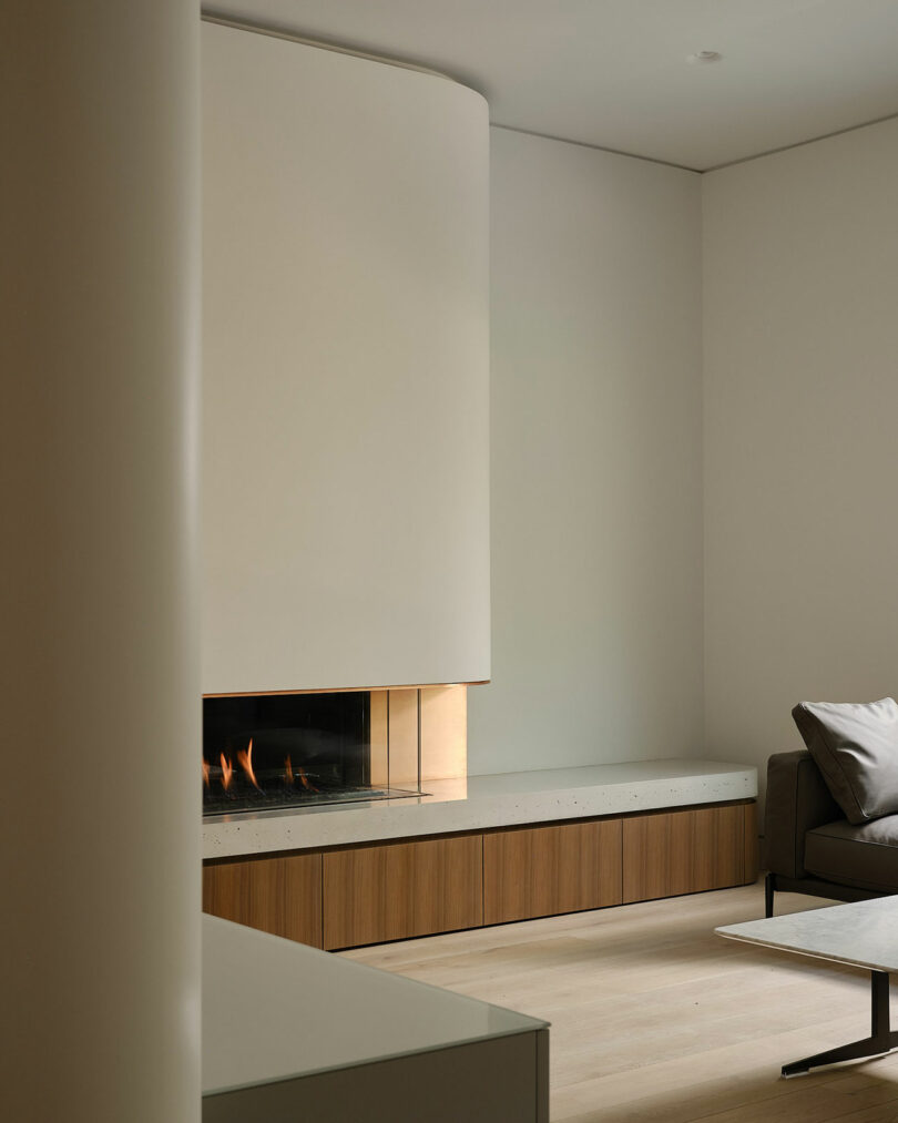Minimalist living room with a contemporary fireplace, light wooden floor, gray sofa, and a low-built wooden shelf.