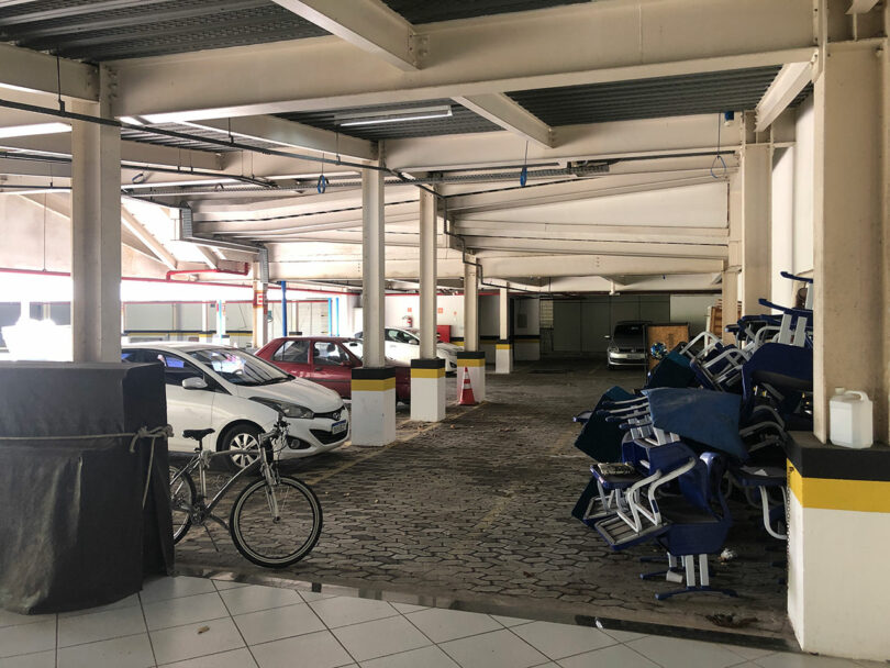 A parking garage with white walls and several parked cars. There are a few bicycles in the background.