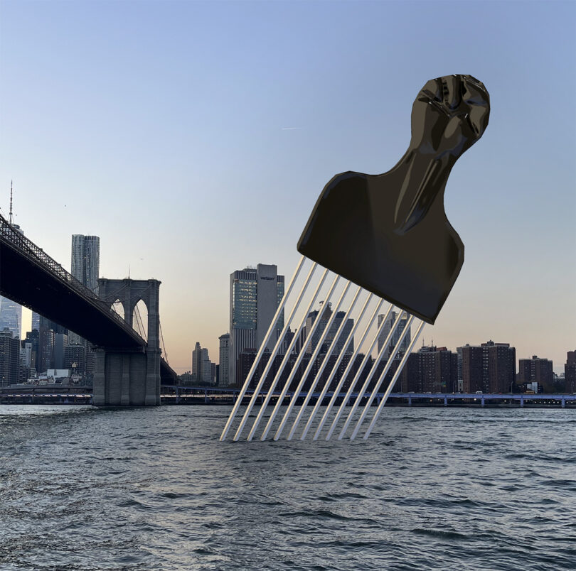 A giant hair pick sculpture with a clenched fist handle is installed in a river, with a city skyline and a bridge visible in the background.