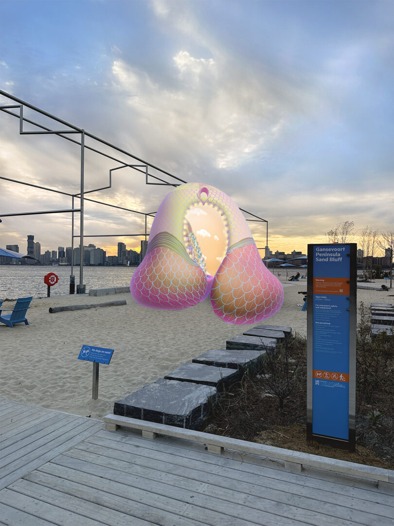 A large, pink and yellow abstract sculpture is situated on a sandy waterfront area with a skyline in the background. An information board is in the foreground near a wooden walkway.
