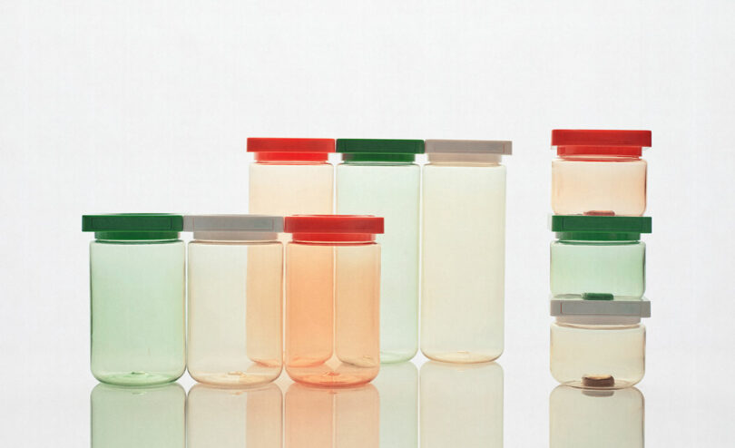 An assortment of transparent jars with colorful lids, arranged in a neat group on a reflective surface. Some lids are red, green, or gray. Three jars are stacked on the right.