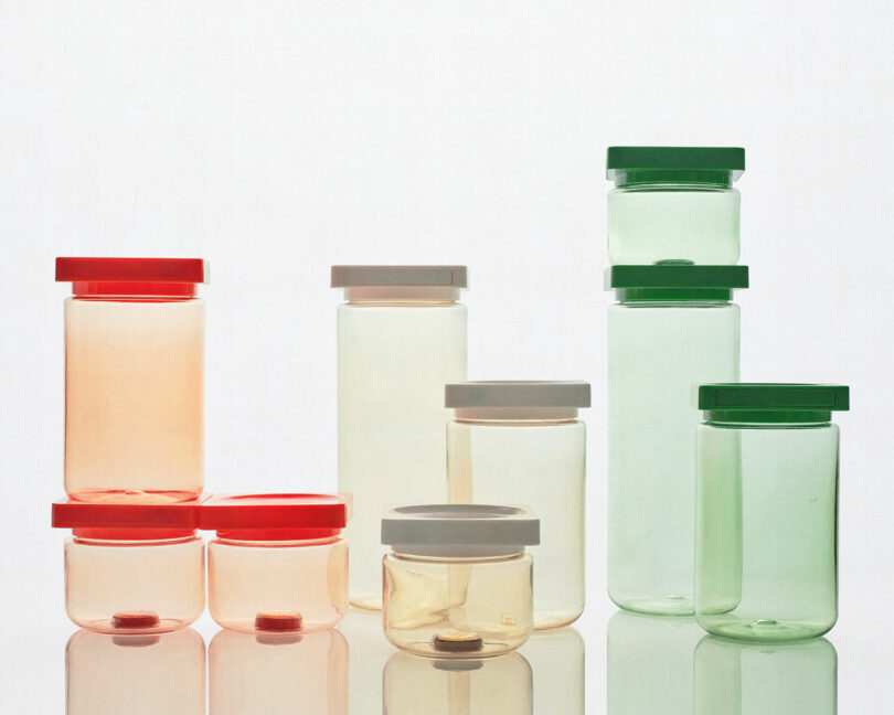 Various sizes of transparent plastic containers with different colored lids (red, gray, and green) are arranged on a reflective surface against a white background.