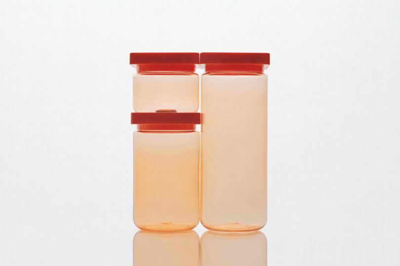Four orange-tinted, cylindrical storage containers with red lids, arranged in a staggered manner against a plain white background.