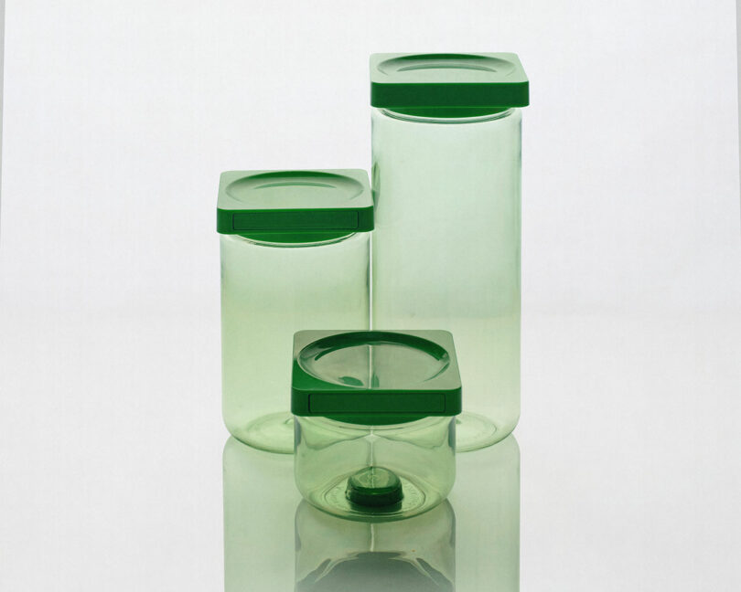 Three transparent green containers with green lids arranged in a staggered formation on a reflective surface.