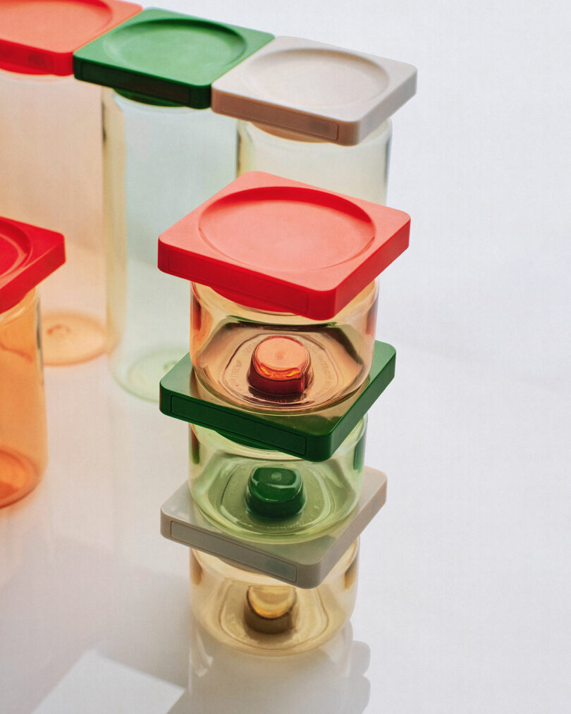 Several clear plastic containers of various sizes with square colored lids (red, green, and white) are stacked and arranged on a white surface.
