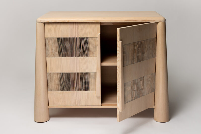 A light wooden cabinet with a partially open door, featuring a simple design and textured paneling on the front.